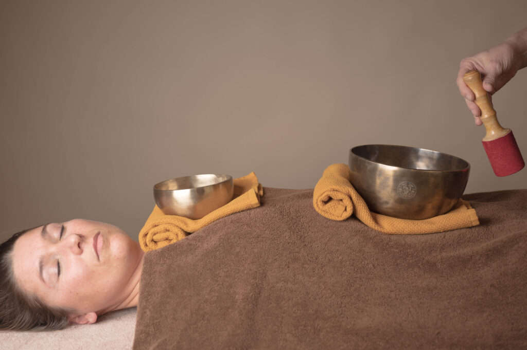 Photo d’une femme allongée sur une table de massage avec des bols chantants sur elle durant une formation massage sonore aux bols tibétains 